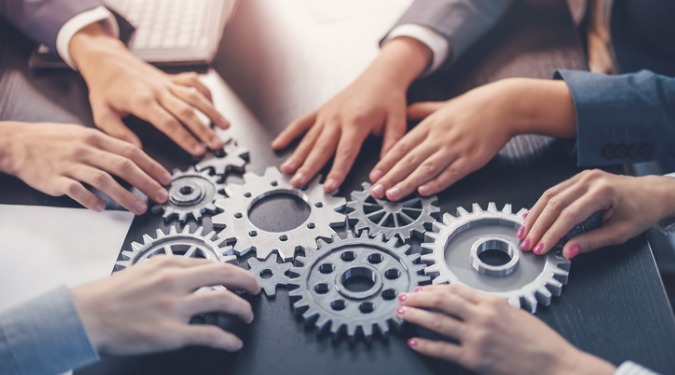 people joining hands on a cog wheel on a desk