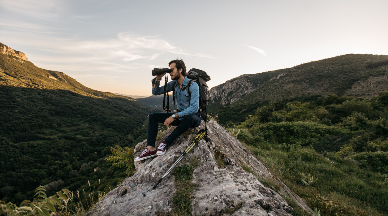 Hiker sitting on rock looking through binoculars